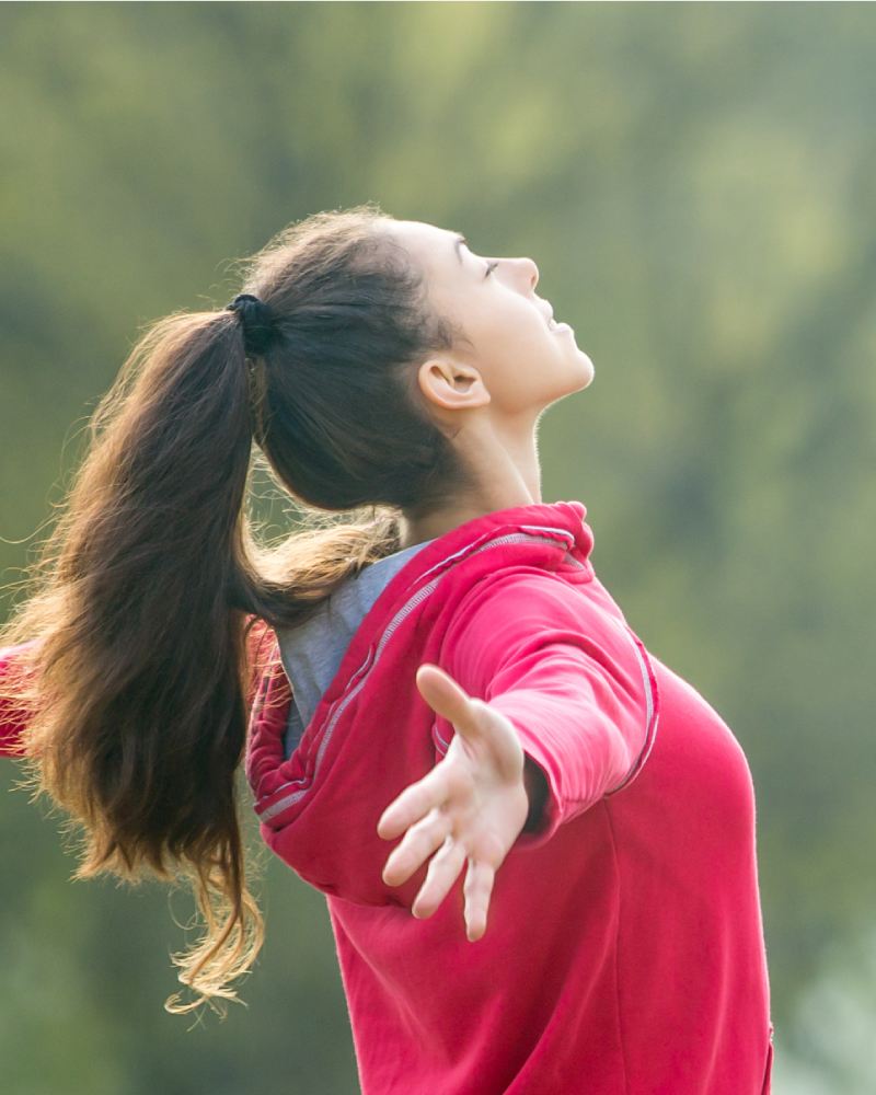 woman with a ponytail in a red hoodie stretching her arms wide and leaning her head back with her eyes closed