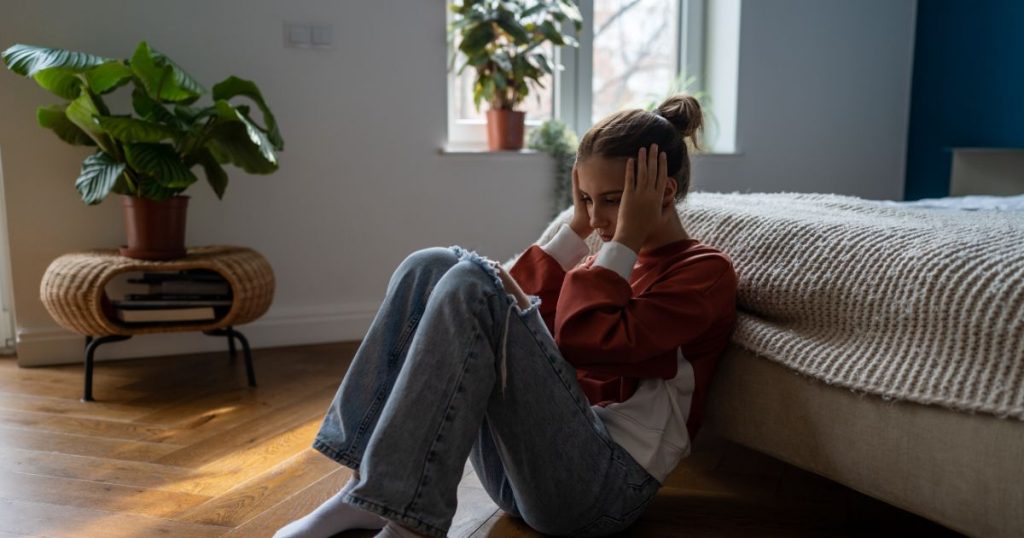 woman sitting on the floor in front of her bed with her head in her hands