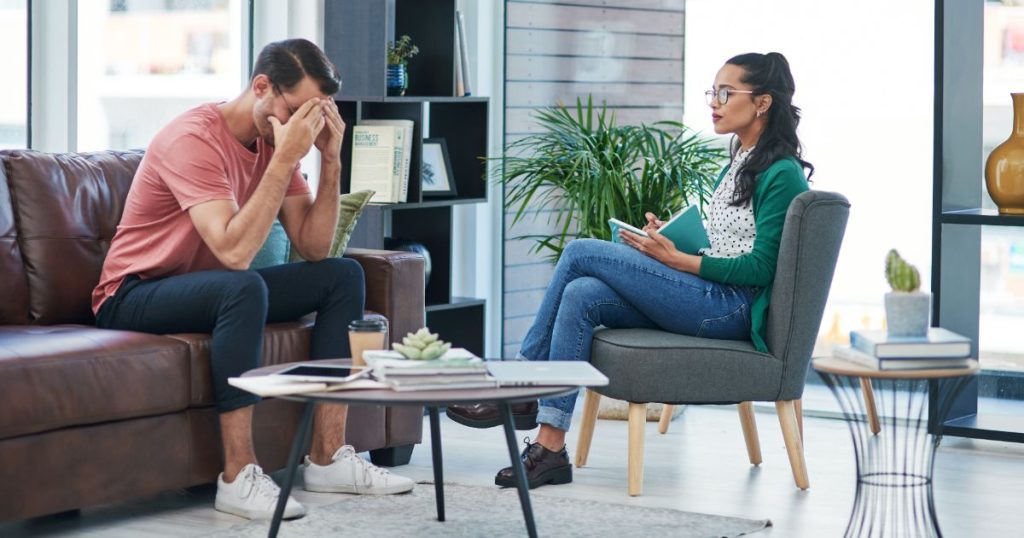 man sitting on couch with his head in hands talking to a therapist