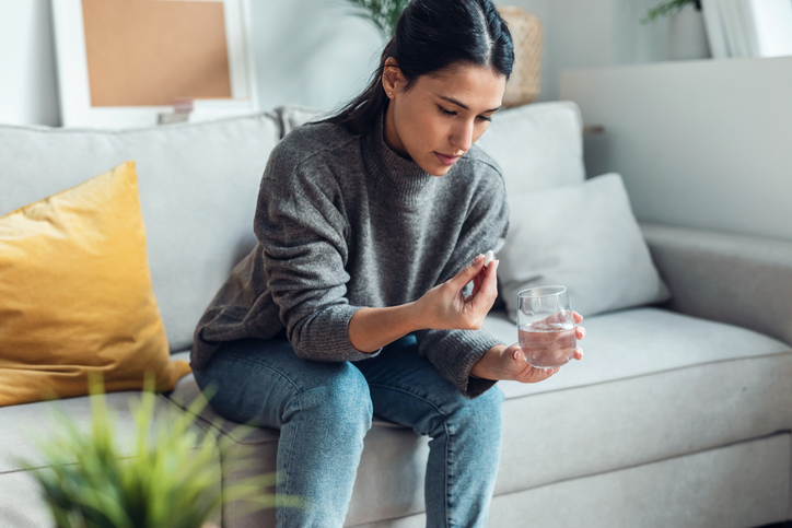 Depressed sad woman taking pills while sitting on couch at home.